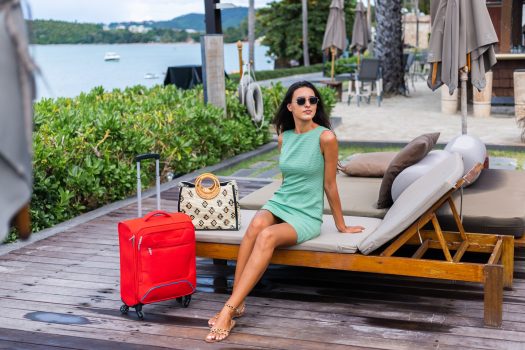 happy-caucasian-pretty-long-hair-elegant-tourist-woman-dress-with-red-suitcase-outside-hotel